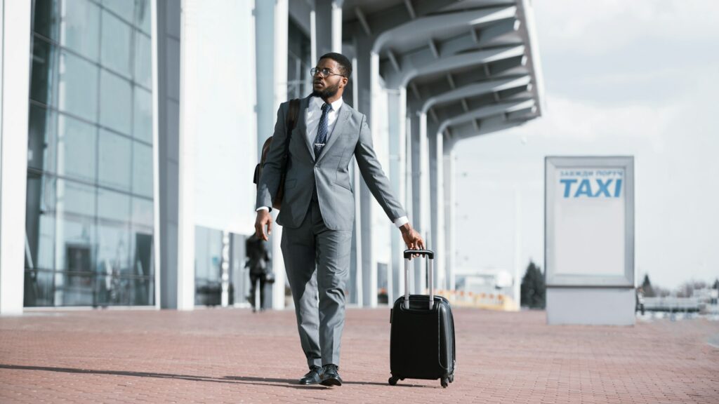 Black Businessman Walking With Suitcase Near Buffalo Express Airport Taxi Parking, Panorama