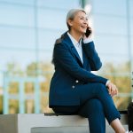 Grey asian woman talking on mobile phone while sitting at buffalo airport parking